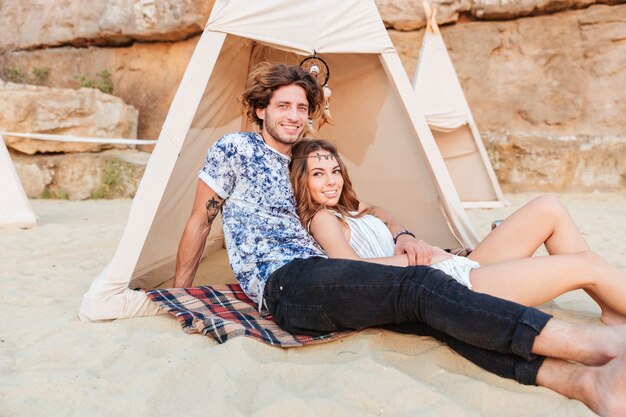 Bella giovane coppia seduta in tepee sulla spiaggia