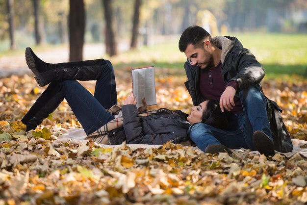 Bella giovane coppia seduta nel parco in una bella giornata autunnale stanno leggendo un libro