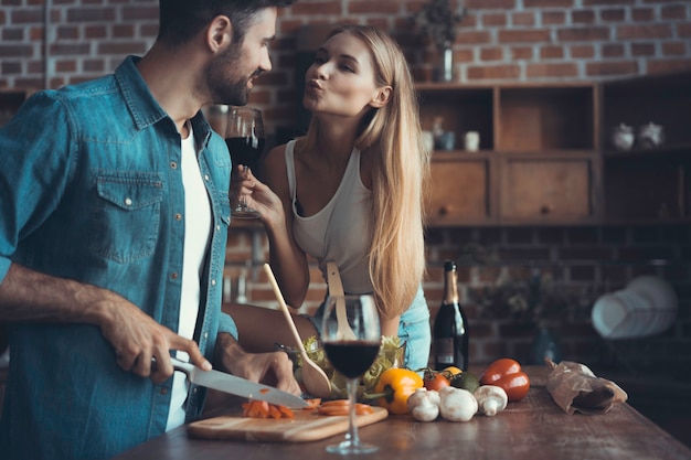 Bella giovane coppia sta bevendo vino e sorridendo mentre cucina in cucina a casa.