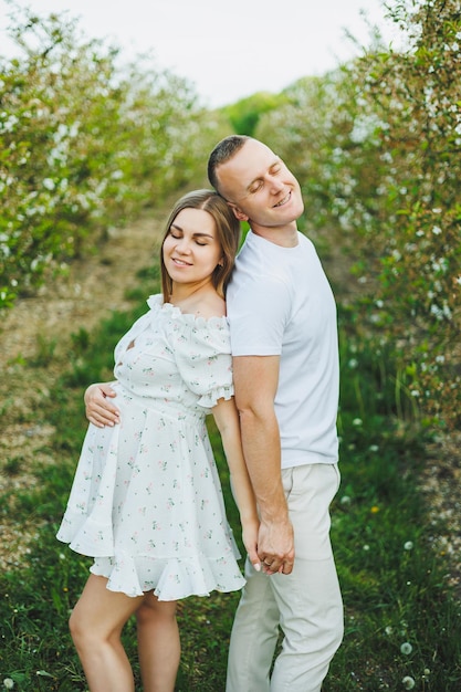 Bella giovane coppia uomo e donna incinta nel giardino primaverile Concetto di famiglia stile di vita di bellezza Una madre felice aspetta un bambino Una giovane coppia felice in un giardino fiorito