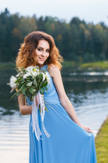 Bella giovane damigella d'onore in posa vicino al lago il giorno del matrimonio