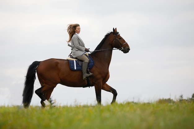 Bella giovane donna a cavallo sul campo Lateralmente alla fotocamera Movimento di gioia di libertà