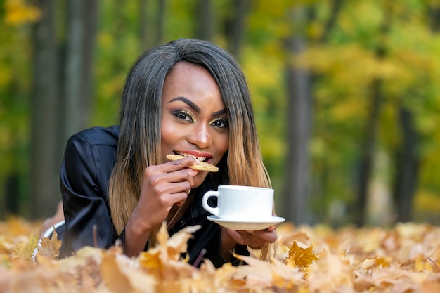 Bella giovane donna africana che mangia i biscotti e che beve caffè nella foresta