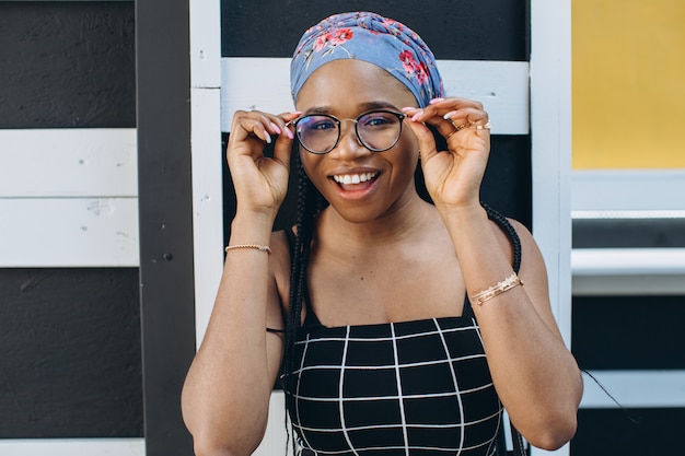 Bella giovane donna africana con gli occhiali che indossa abito alla moda in posa sulla strada. Acconciatura afro