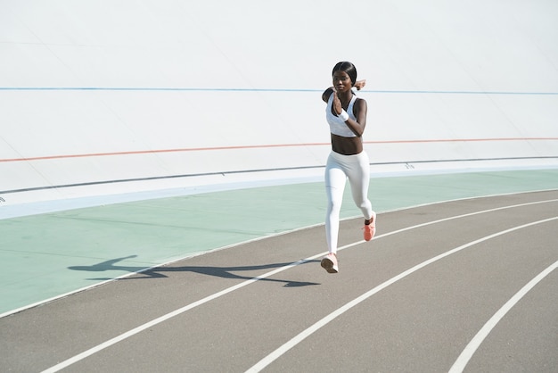 Bella giovane donna africana in abbigliamento sportivo che corre in pista all'aperto