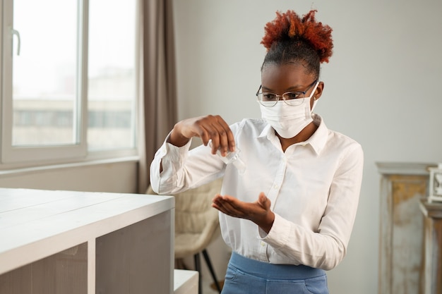 bella giovane donna africana in bicchieri in una mascherina medica con un antisettico nelle sue mani