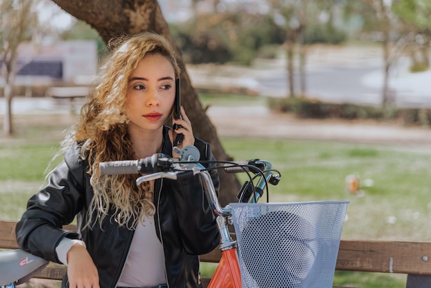Bella giovane donna all'aperto nel parco con la bicicletta bella giornata di primavera utilizzando il telefono cellulare