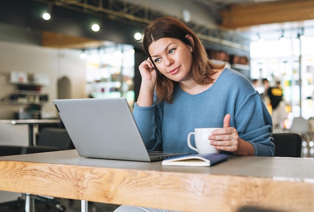 Bella giovane donna alla moda plus size corpo positivo utilizzando il laptop presso l'ufficio del salone di bellezza piccolo