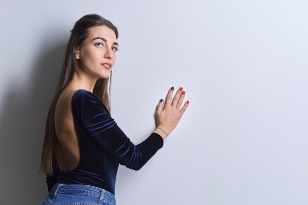 Bella giovane donna alla moda su fondo bianco, femmina in vestiti blu, jeans. Femmina che guarda l'obbiettivo, posto pulito per il testo, copia spazio