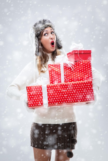 Bella giovane donna allegra in abiti caldi che tengono molti regali di Natale mentre nevica.