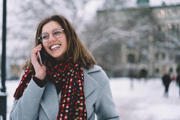 Bella giovane donna allegra in abito invernale parlando al cellulare in strada con la neve