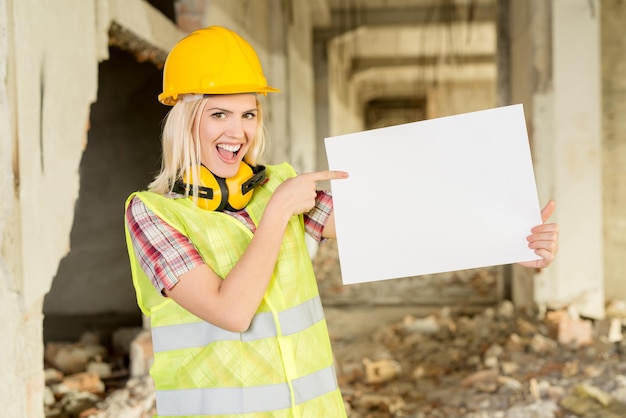 Bella giovane donna architetti edili nell'edificio danneggiato nel disastro. Lei indica una lavagna bianca vuota e sorride guardando la fotocamera.