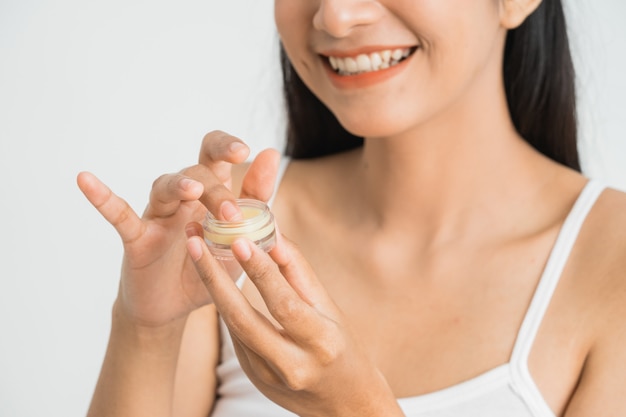 Bella giovane donna asiatica che applica crema cosmetica sul viso. Balsamo per le labbra