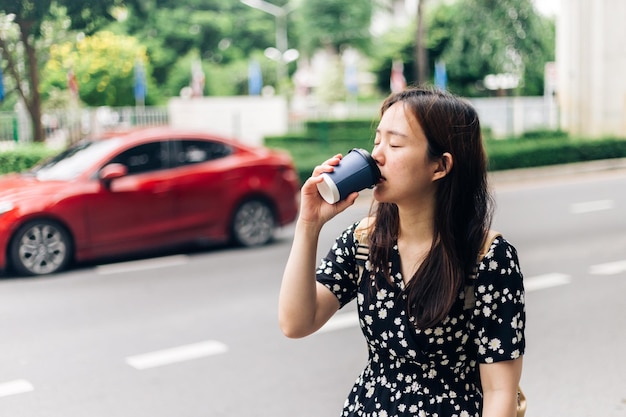 Bella giovane donna asiatica che beve caffè sulla strada della città