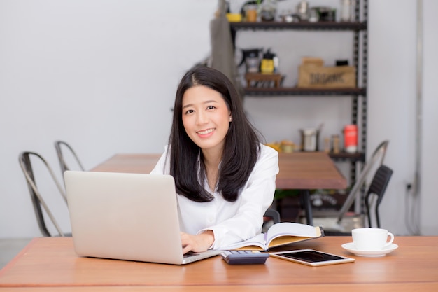 Bella giovane donna asiatica che lavora online sul computer portatile che si siede alla caffetteria.