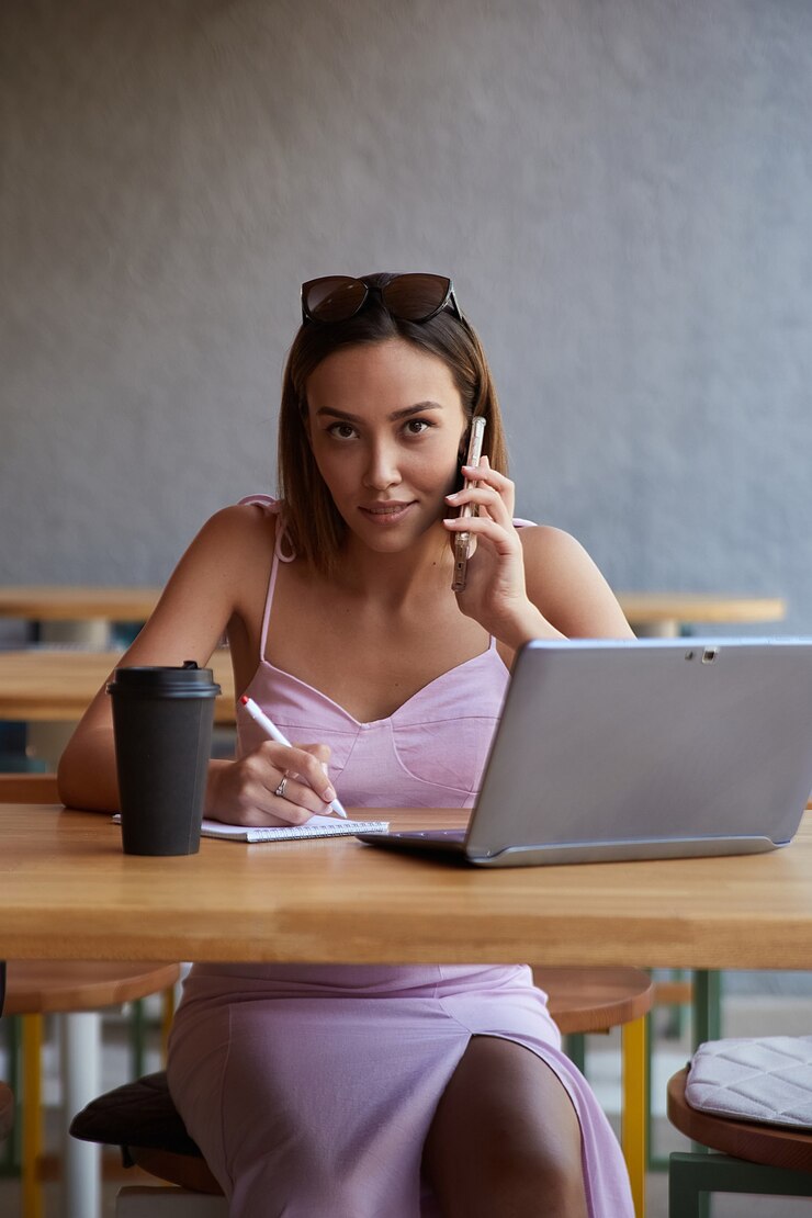 Foto bella giovane donna asiatica che si siede con il computer portatile al caffè che chiama dallo smartphone