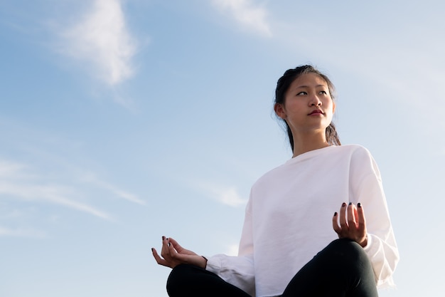 Bella giovane donna asiatica che si siede meditando