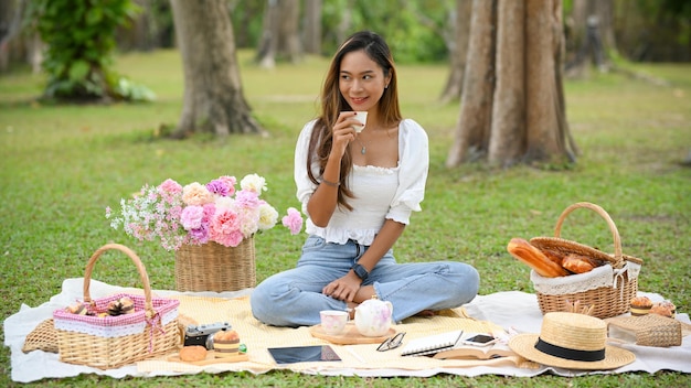 Bella giovane donna asiatica che sorseggia un tè facendo un picnic in una bella giornata estiva nel parco verde