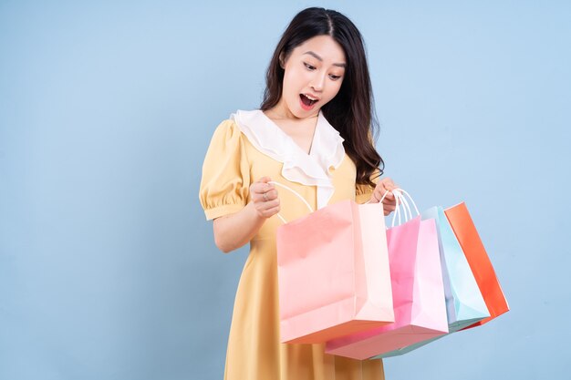 Bella giovane donna asiatica che tiene la borsa della spesa su sfondo blu