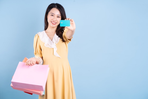 Bella giovane donna asiatica che tiene la borsa della spesa su sfondo blu