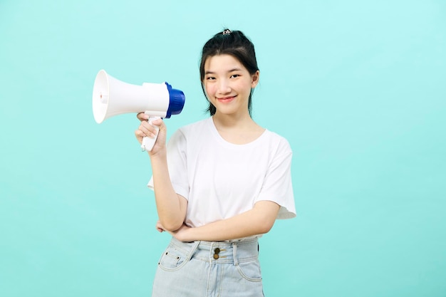 Bella giovane donna asiatica che tiene megafono su sfondo blu studio