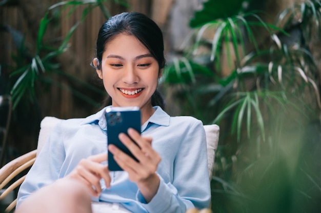 Bella giovane donna asiatica che utilizza il telefono in giardino