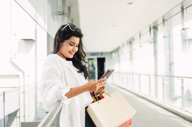 bella giovane donna asiatica con le borse della spesa utilizzando smartphone nel centro commerciale