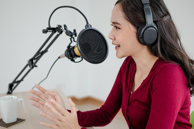 Bella giovane donna asiatica conduttrice radiofonica che lavora in cuffia, microfono mentre parla, conversa e registra podcast, in diretta sui social media. Tecnologia di on-air online nella trasmissione in studio.