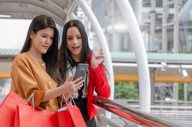 bella giovane donna asiatica e caucasica con smart phone mobile, carta di credito e borse della spesa