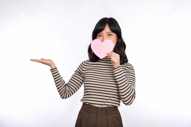 Bella giovane donna asiatica in possesso di un cuore di carta, mentre in piedi su sfondo bianco Bella giovane donna asiatica con cuore di carta