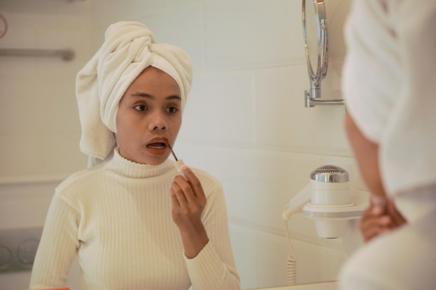 Bella giovane donna asiatica in veste bianca che fa trucco in bagno davanti al grande specchio