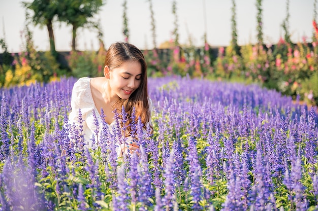 Bella giovane donna asiatica in vestito bianco profumato fiori di lavanda in giardino soleggiato