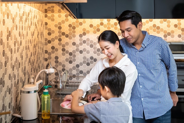 Bella giovane donna asiatica madre con uomo marito e giovane ragazzo figlio famiglia lavare i piatti nella moderna cucina che guarda l'obbiettivo