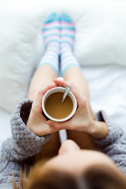 Bella giovane donna bere il caffè sul letto.