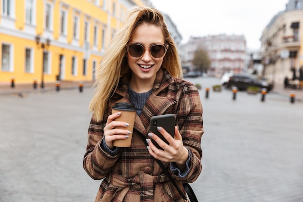 Bella giovane donna bionda alla moda che indossa un cappotto che cammina all'aperto