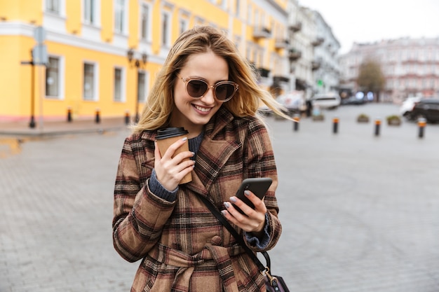 Bella giovane donna bionda alla moda che indossa un cappotto che cammina all'aperto