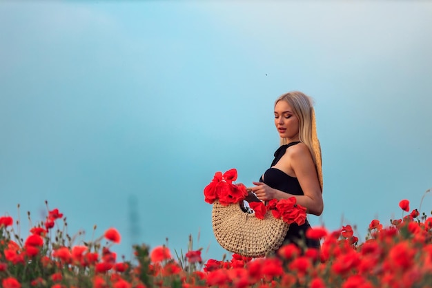 Bella giovane donna bionda cammina su un campo fiorito di papaveri al tramonto