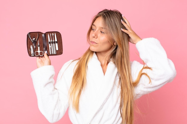 Bella giovane donna bionda che indossa accappatoio e tiene in mano una borsa per il trucco con strumenti per unghie