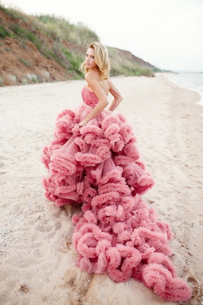 Bella giovane donna bionda che porta vestito rosa sulla spiaggia