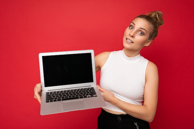 Bella giovane donna bionda con i capelli raccolti che guarda l'obbiettivo che tiene il computer portatile