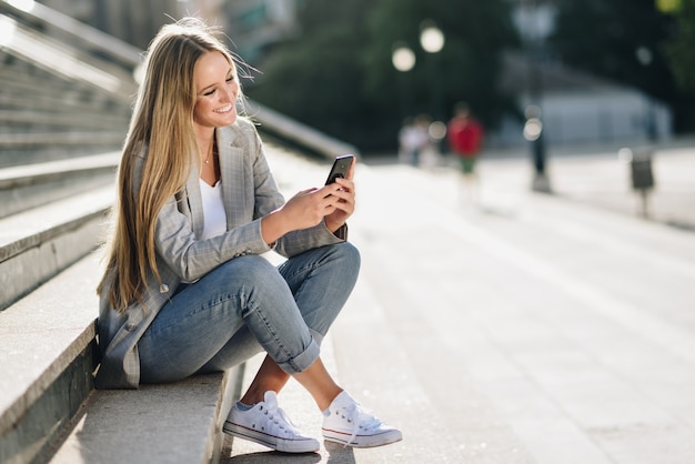 Bella giovane donna bionda guardando il suo smartphone e sorridente.