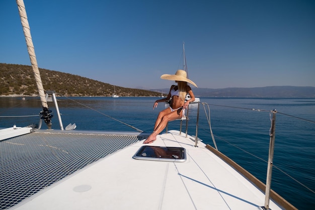 Bella giovane donna bionda in bikini che si siede sulla prua del catamarano alla soleggiata giornata estiva