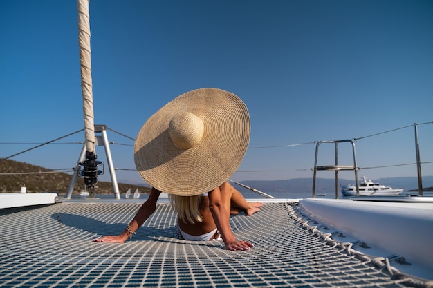 Bella giovane donna bionda in bikini che si siede sulla prua del catamarano alla soleggiata giornata estiva