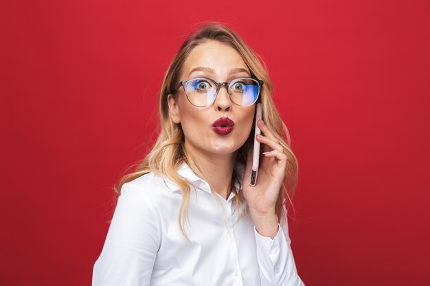 Bella giovane donna bionda in piedi isolato su sfondo rosso, tenendo il telefono cellulare