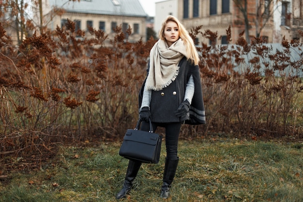 Bella giovane donna bionda in un elegante cappotto autunnale con una borsa nera alla moda