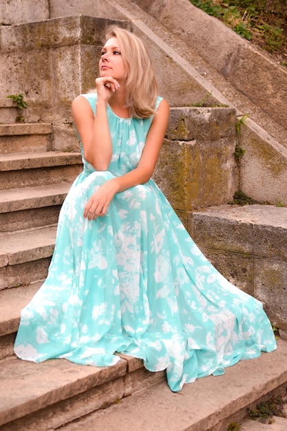 Bella giovane donna bionda in un vestito in un parco cittadino in estate