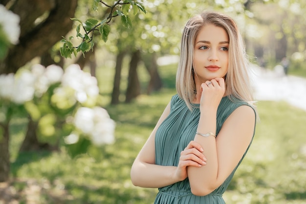 Bella giovane donna bionda in vestito verde nel giardino dei fiori di primavera