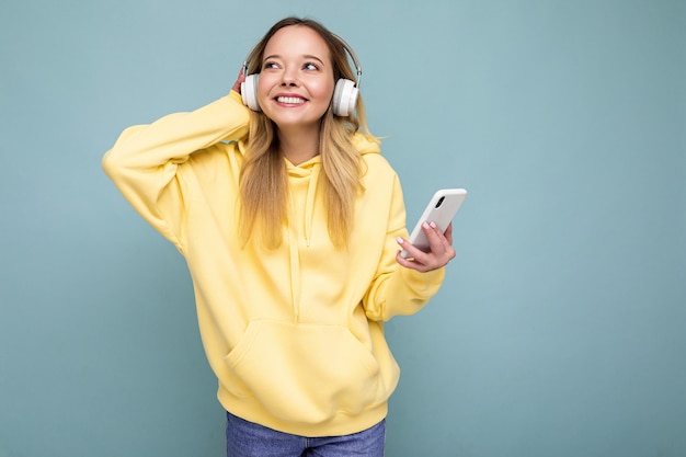 Bella giovane donna bionda positiva che indossa la felpa con cappuccio alla moda gialla isolata