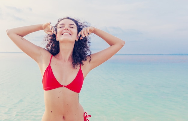 Bella giovane donna castana felice riccia affascinante in un bikini rosso al mare