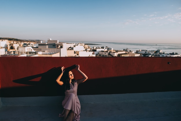 Bella giovane donna castana in un vestito da sera bianco. ambientazione sullo sfondo del tramonto della città.